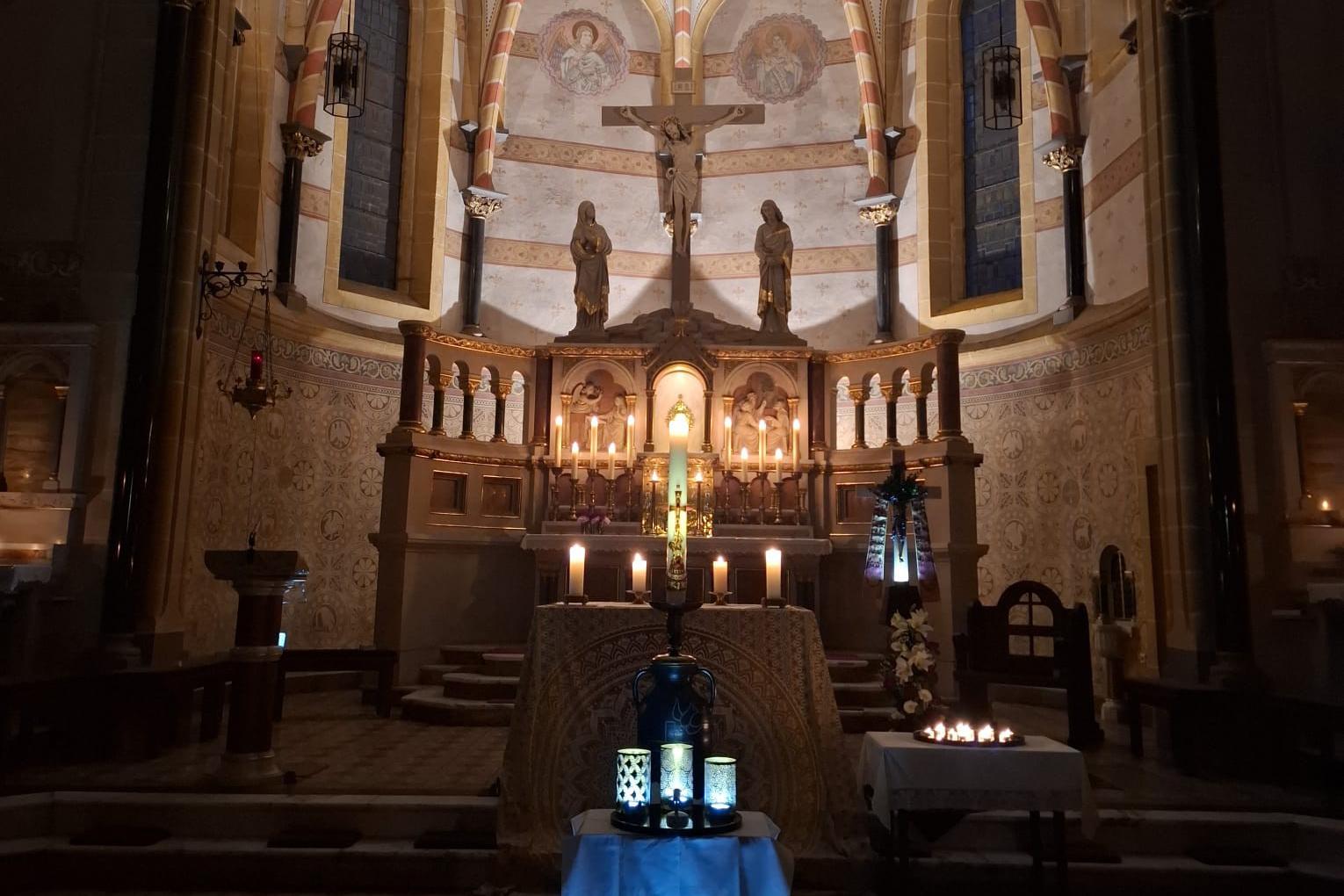 Ein festlich beleuchteter Kirchenaltar mit Kerzen und Kreuz im Zentrum.
