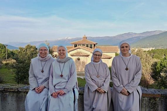 Vier Ordensschwestern vor einem Kloster in bergiger Landschaft.