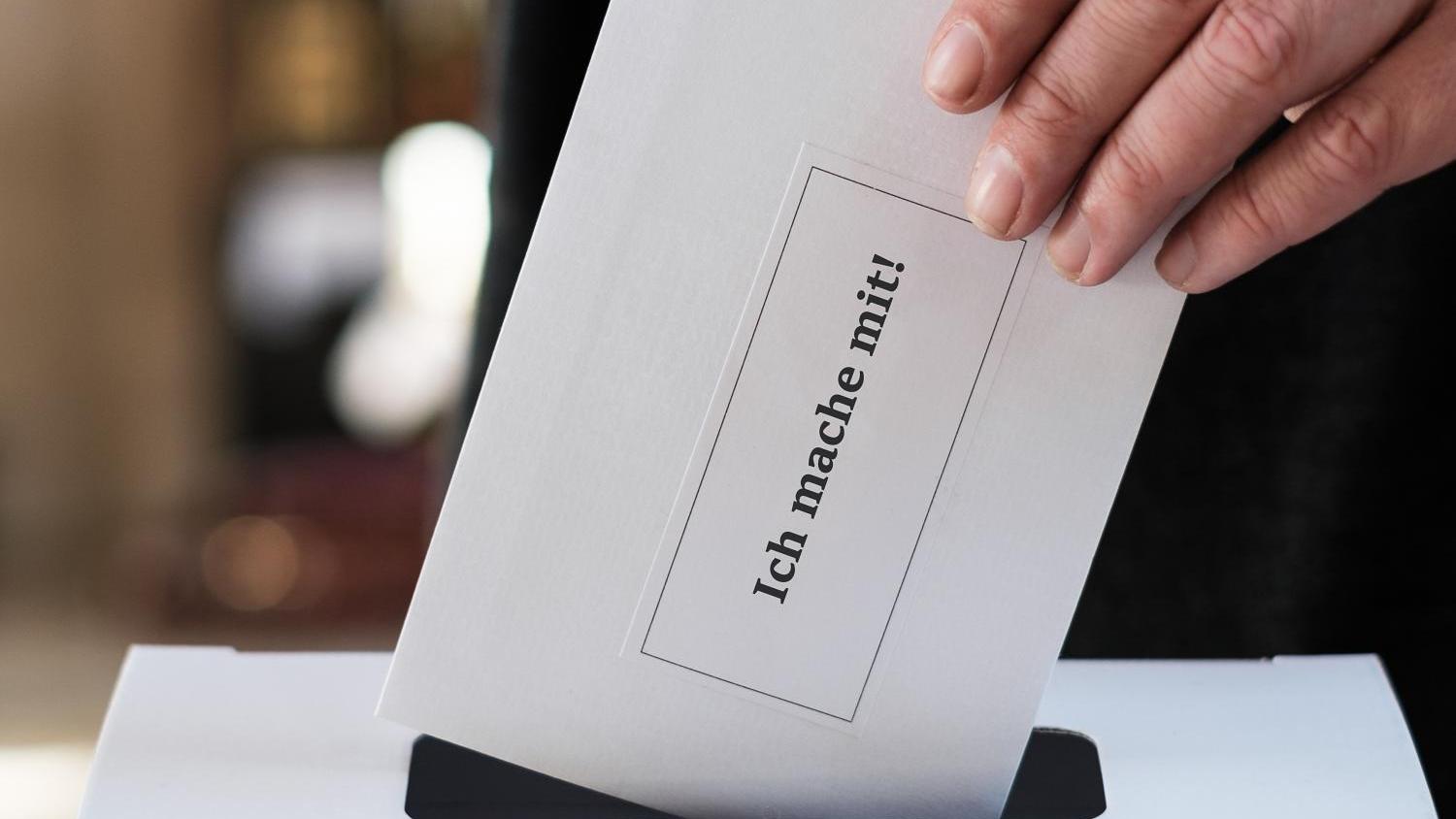 Hand wirft Wahlzettel in eine Wahlurne