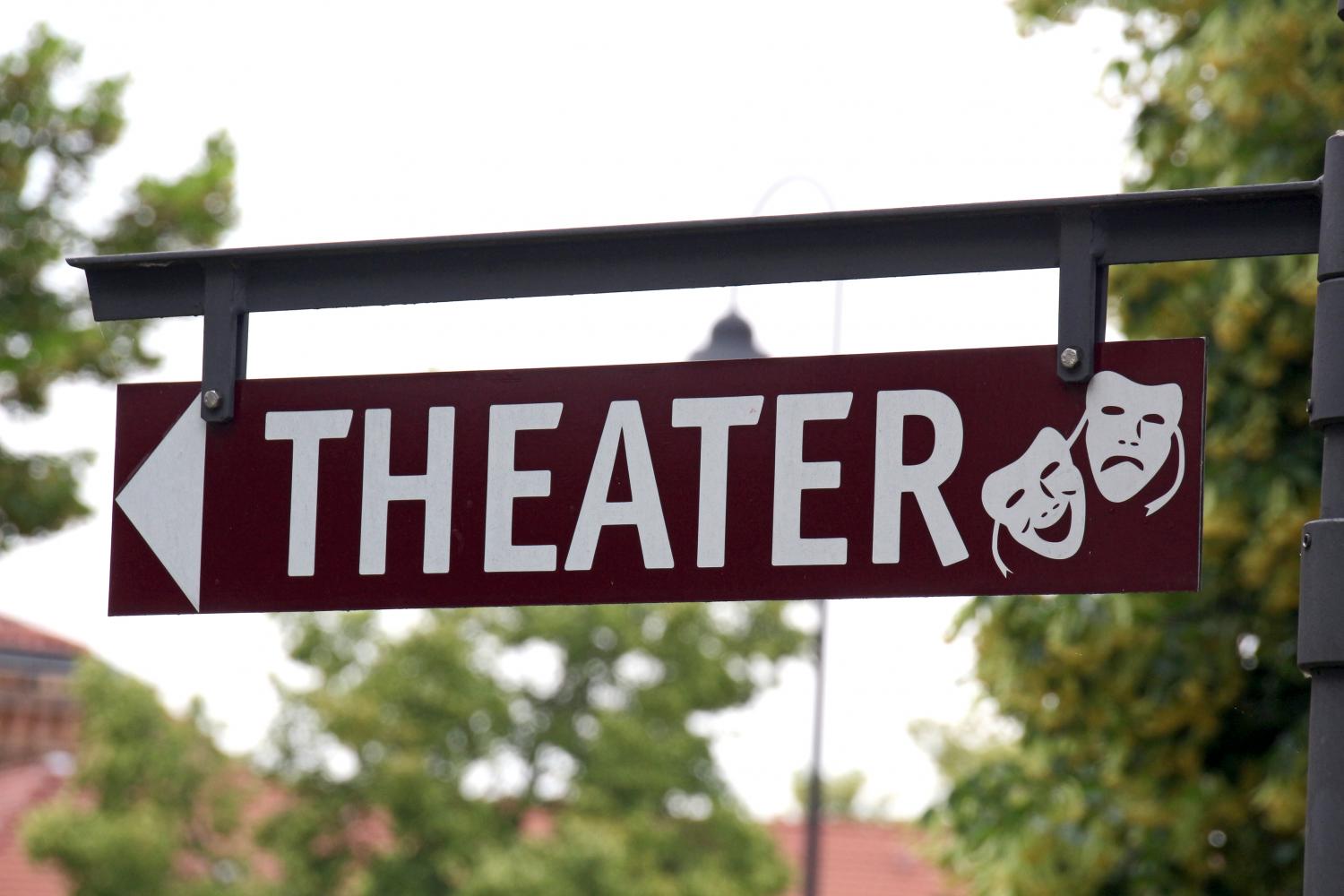 Ein Wegweiser mit der Aufschrift „THEATER“ zeigt nach links; daneben sind zwei typische Theatermasken für Komödie und Tragödie abgebildet.