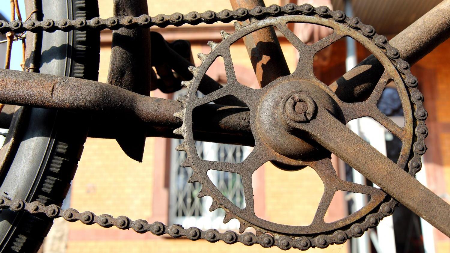 Das Bild zeigt eine rostige Fahrradkette, ein großes Kettenrad und Teile des Hinterrads, alles stark verrostet und verwittert.