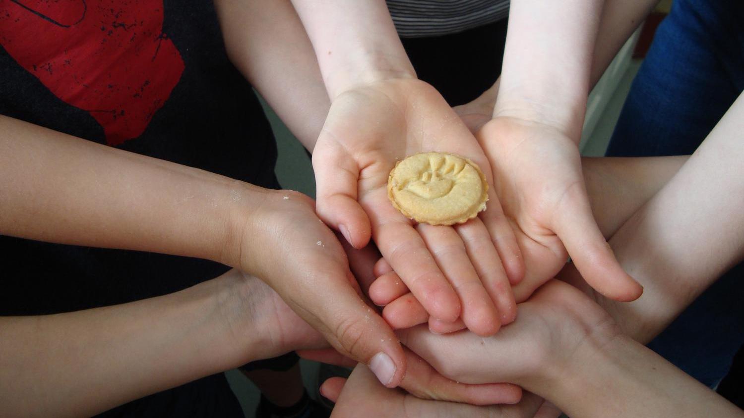 Mehrere Kinderhände halten gemeinsam einen Keks mit dem Symbol einer Pfingsttauben