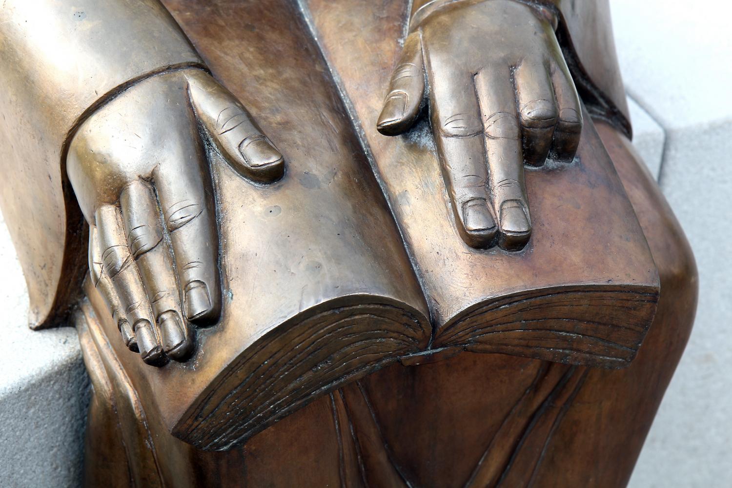 Eine bronzene Skulptur zeigt zwei Hände, die auf einem geöffneten Buch ruhen.
