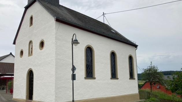 Eine kleine, weiß verputzte Dorfkirche mit schmalen Rundbogenfenstern und steilem Schieferdach.